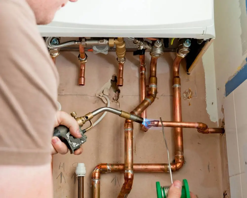 A man is working on pipes in the wall.