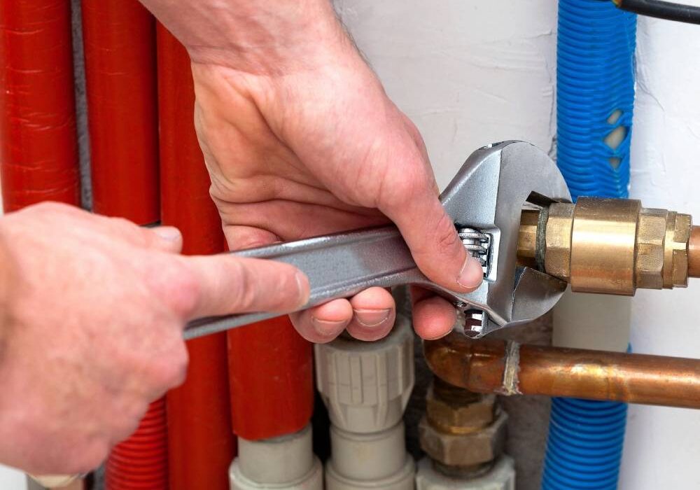 A person holding a wrench over the water heater.